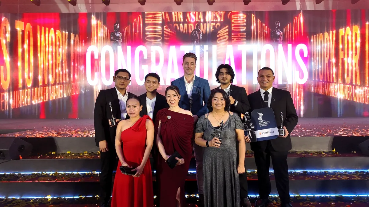 Eight members of the OutForce team on stage at the HR Asia Best Companies to Work for in Asia 2026 awards, holding five trophies in front of a lit-up "Congratulations" screen